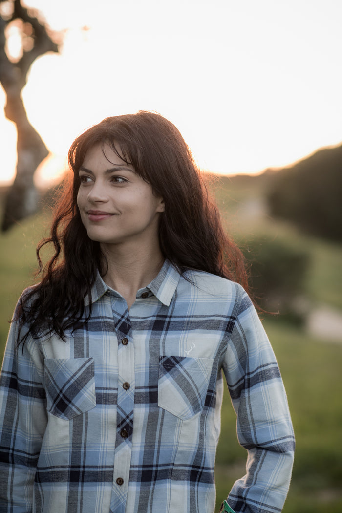 Woman in Pladra's Women's Every Day Double Weave Shirt—Birch White smiles outdoors at sunset.