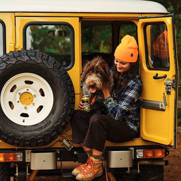 Woman in Pladra's Women's Every Day Elite Flannel Shirt-Bighorn Blue sits in a yellow SUV with her happy dog and a drink.