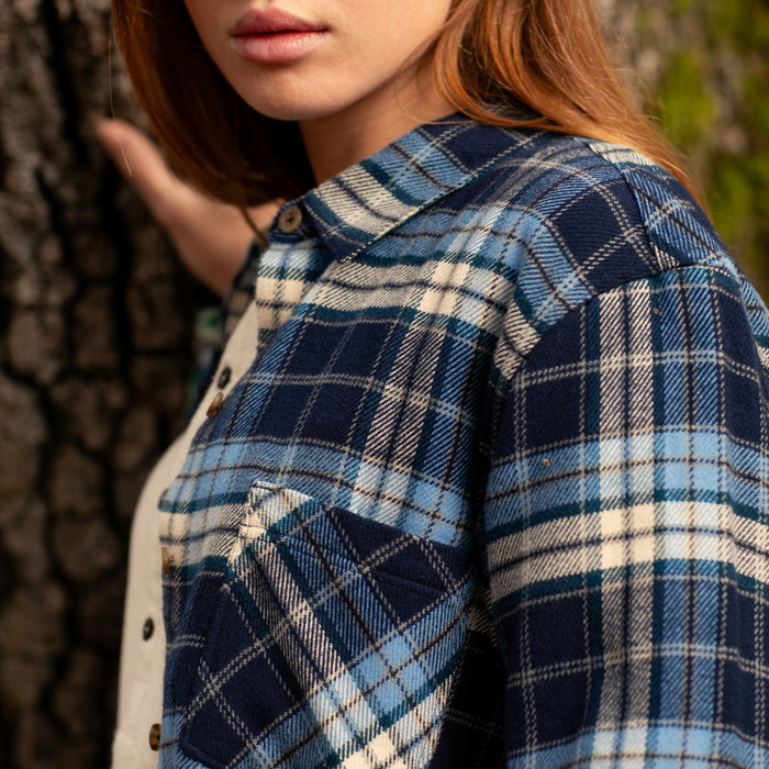 Woman wearing Pladra’s Women's Every Day Elite Flannel Shirt in Bighorn Blue enjoys the outdoors by a tree.