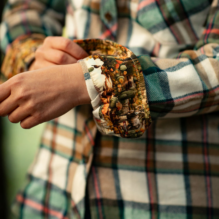 Someone adjusts the cuff of a Pladra Women's Every Day Elite Flannel Shirt in Coyote Tan, showing the patterned lining.