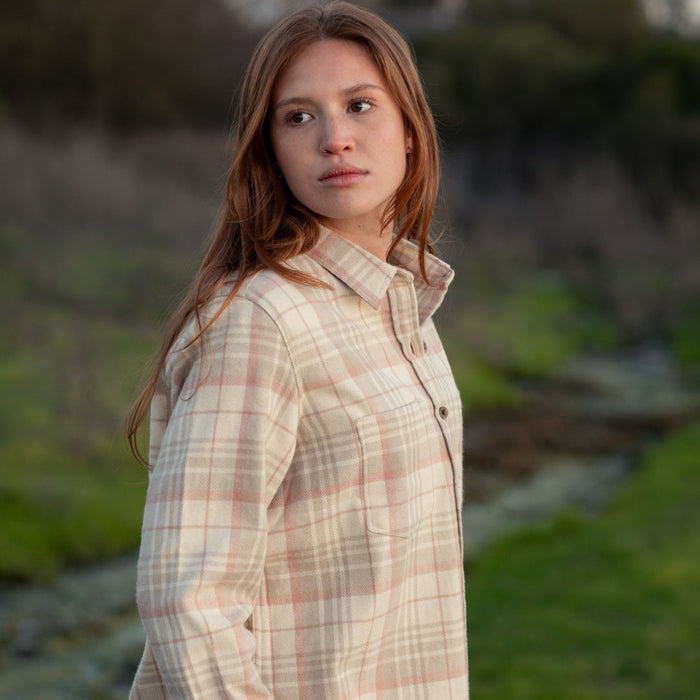 A woman with long reddish-brown hair wears the Women's Every Day Elite Flannel Shirt in Lighthouse White, standing outdoors on green grass. She looks calmly to her left, with blurred trees and grass in the background.