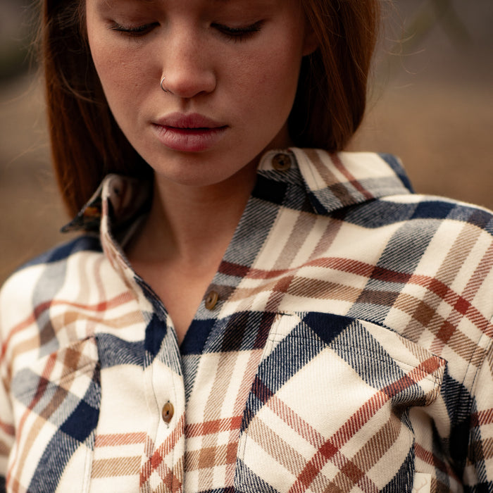 A woman in a Pladra Women's Every Day Elite Flannel Shirt—Whitefish Tan—looks down, her hair loose and nose ring visible.