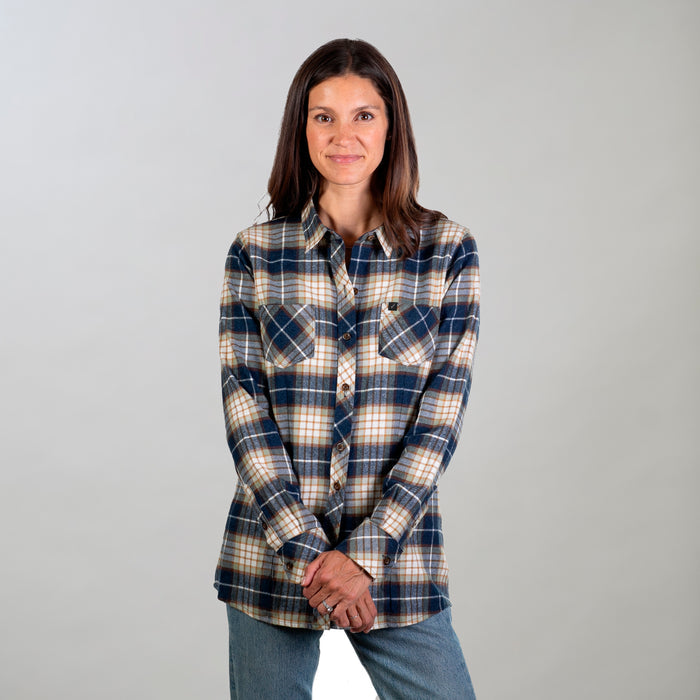 A woman with straight brown hair stands against a light background, wearing the Women's Every Day Flannel Shirt- Banff Blue and blue jeans, hands clasped in front of her and smiling slightly.