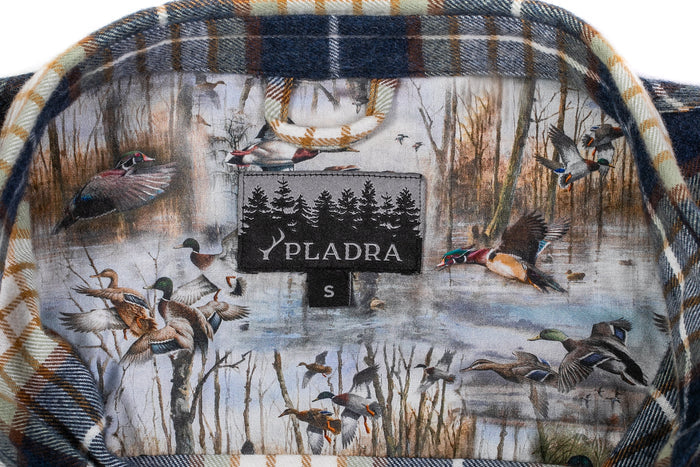 Close-up of the Women's Every Day Flannel Shirt- Banff Blue collar, featuring a Pladra label. Crafted from premium cotton, its inner fabric displays ducks in a marsh, with plaid flannel peeking along the collar edge.