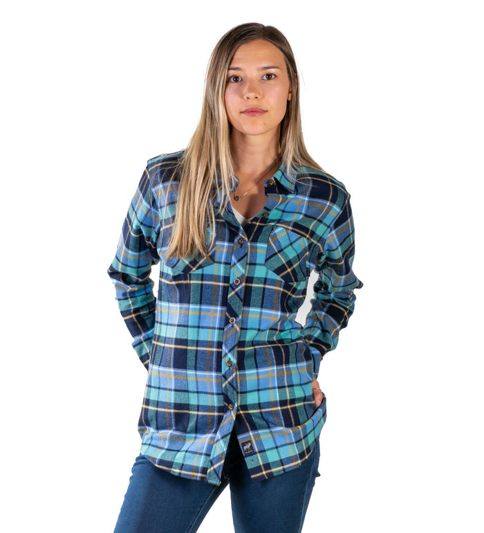 A woman with straight, light brown hair wears the Women's Every Day Flannel Shirt in Bay Blue and dark jeans, standing with one hand in her pocket against a plain white background.