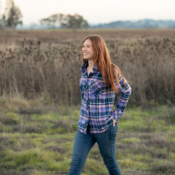 A woman with long red hair smiles in a Pladra Women's Every Day Flannel Shirt–Blackberry Purple and jeans outdoors.