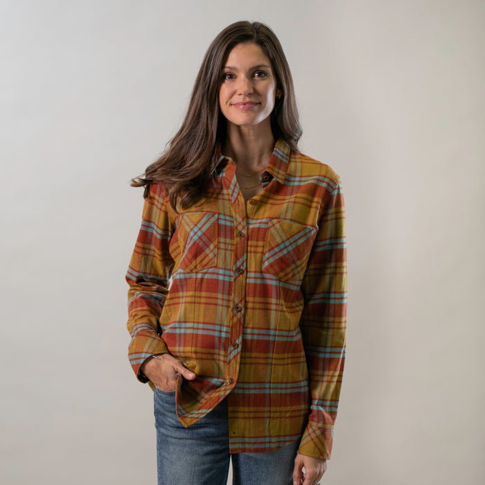 A woman with long brown hair stands against a plain light background, smiling slightly with one hand in her pocket while wearing the Women's Every Day Flannel Shirt - Cottonwood Orange.