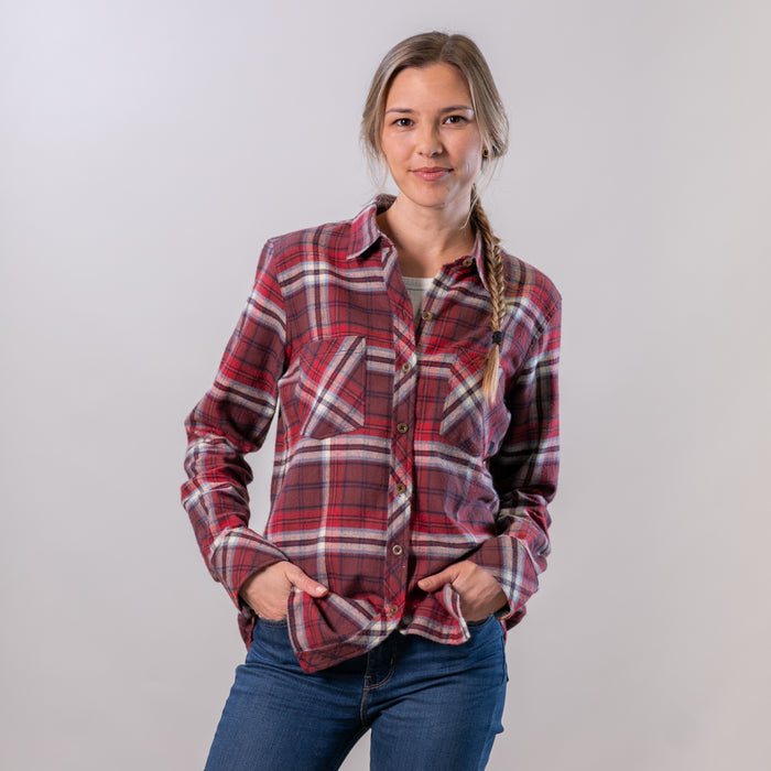 Woman wears Pladra Women's Every Day Flannel Shirt in Harvest Red with jeans, smiling hands-in-pockets against plain backdrop.