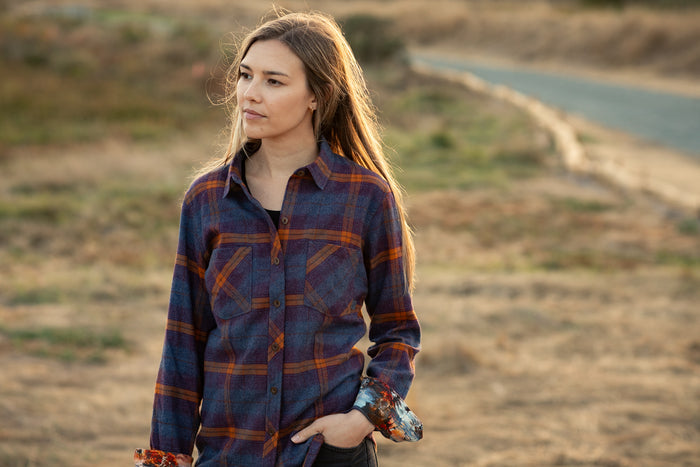 A woman wears the Pladra Women's Every Day Flannel Shirt in Portsmouth Blue Heather, standing outdoors on a dirt path.