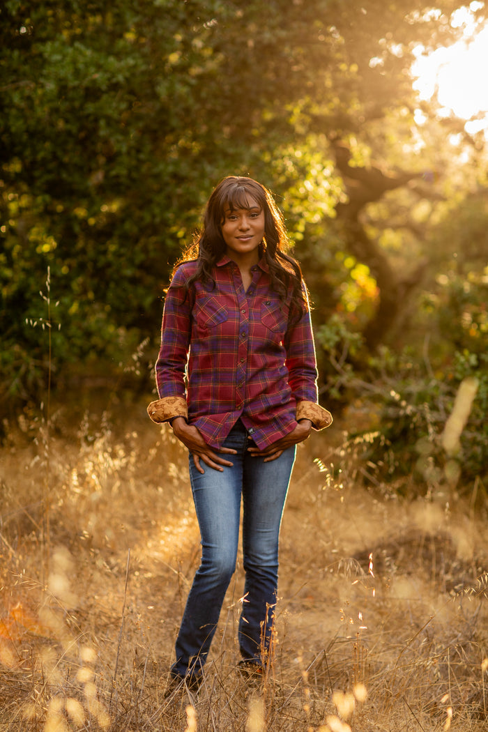 A woman wears the Pladra Women's Every Day Flannel Shirt in RK Plum Red, standing in a sunlit field with tall grass.
