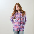 A young woman with long red hair wears a Pladra Women's Every Day Flannel Shirt in Wildflower Pink and jeans.