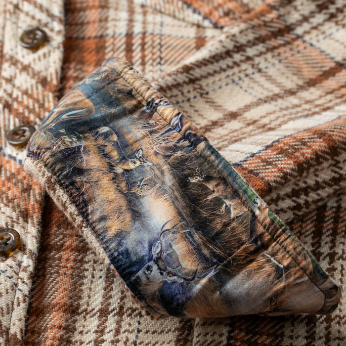 Close-up of the Women's Fireside Flannel in Cattail Tan, featuring rolled cuffs that reveal a contrasting fabric with a deer-in-forest print—crafted from heavyweight Portuguese flannel in warm brown, beige, and orange tones.