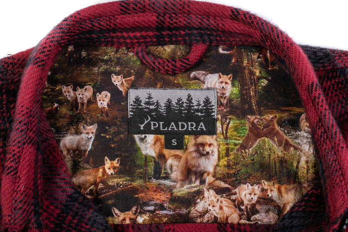 Close-up of the Women's Fireside Flannel- Deadwood Red jacket's collar in red and black plaid, lined with a fox forest print. The “PLADRA S” label with black trees sits on heavyweight Portuguese flannel for warmth.