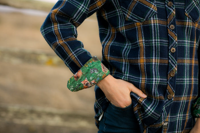 Woman wearing Pladra's Women's Fireside Flannel in Feather Blue with green cuffs, hand in jeans pocket outdoors.