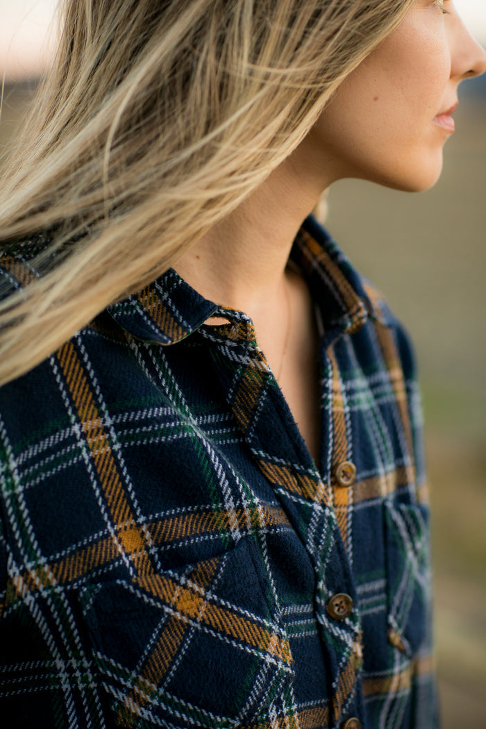 A woman wears the Pladra Women's Fireside Flannel in Feather Blue, blond hair blowing, facing right outdoors.