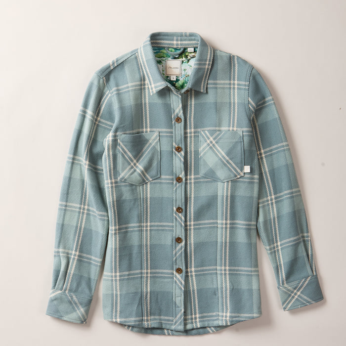 The Women's Fireside Flannel- Island Blue is a long-sleeve, button-up shirt featuring a light blue and white plaid pattern, crafted from organic cotton flannel with two chest pockets and brown buttons.