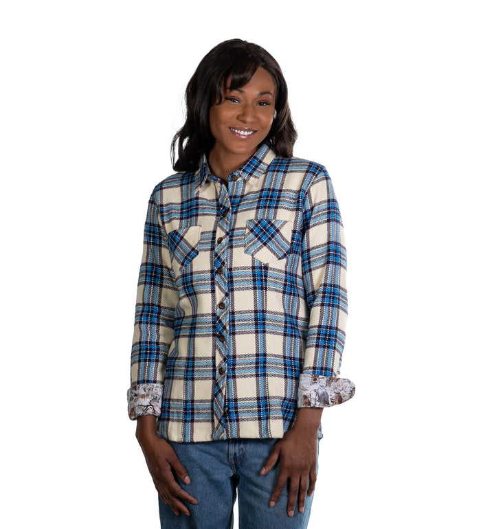 Smiling woman in a Pladra Women's Fireside Flannel- Tahoe Tan shirt and jeans stands against a plain white background.