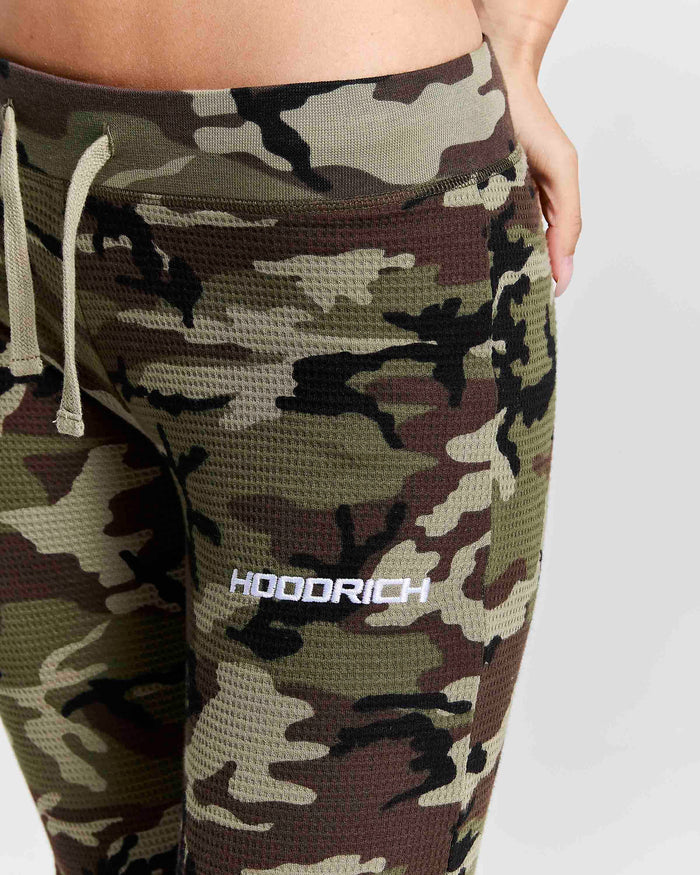 Close-up of a person wearing camouflage waffle-knit leggings with a white drawstring and a white HOODRICH logo on the thigh, against a light gray background.