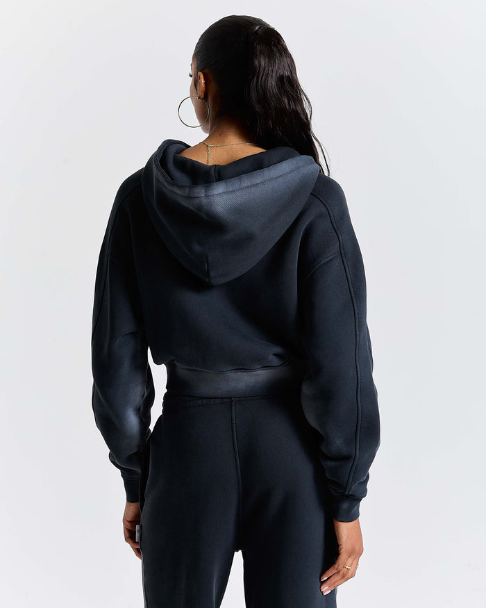 Back view of a model wearing a black cropped zip-up hoodie.