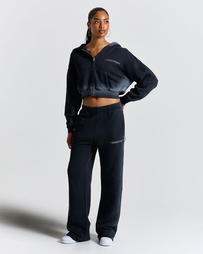 Woman wearing a black tracksuit with brand logo on a light gray background