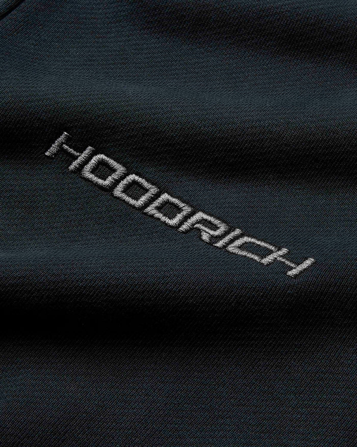 Extreme close-up of the embroidered Hoodrich logo on the black fabric of the hoodie.