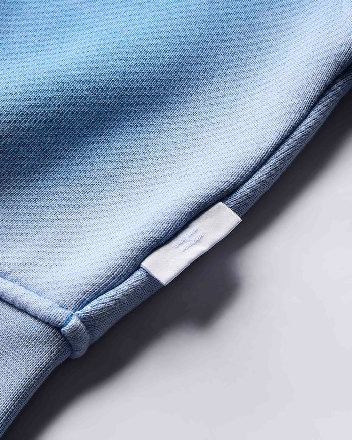 Close-up of the small white branded tab on the side of the blue cropped hoodie.