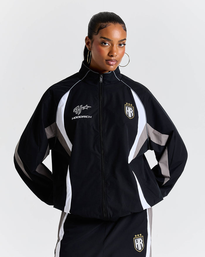 Person wearing a black and white tracksuit with visible branding on a light gray background