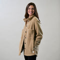 Smiling woman wears Pladra's Women's Headlands Sherpa Shacket in Almond Tan, looking to the side against a plain backdrop.
