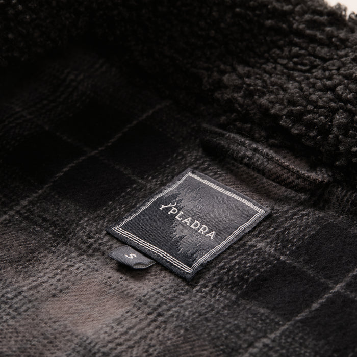 Close-up of the Women's Headlands Sherpa Shacket in Onyx Black, showcasing soft plaid flannel lining. The PLADRA label and small "S" size tag are visible. Perfect for a cozy, stylish Women's Sherpa Shacket look.