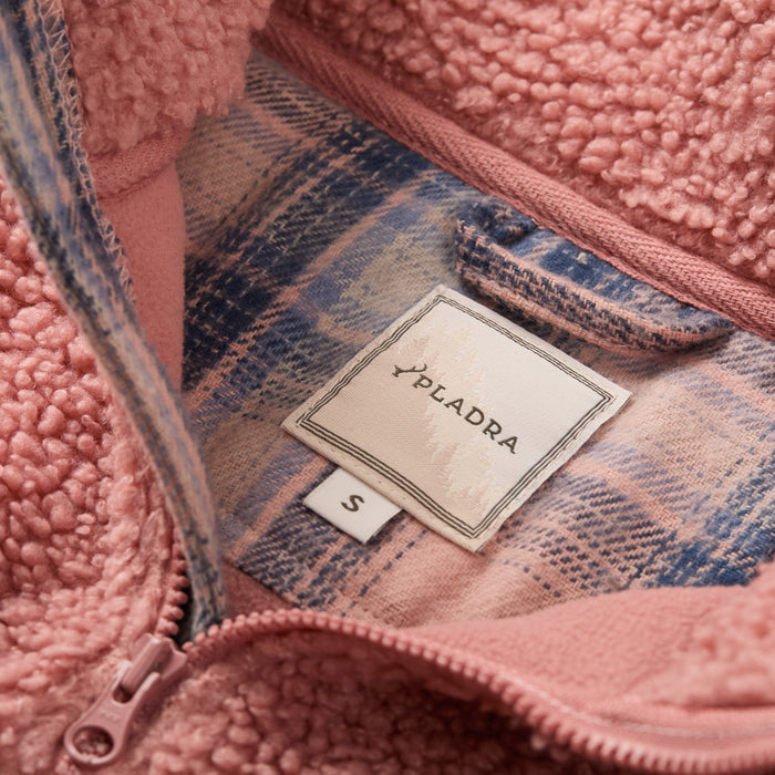 Close-up of the Women's Jenner Sherpa Fleece in coral pink (size S), featuring a zipper, recycled polyester fleece, inner plaid flannel lining, and a PLADRA fabric tag.