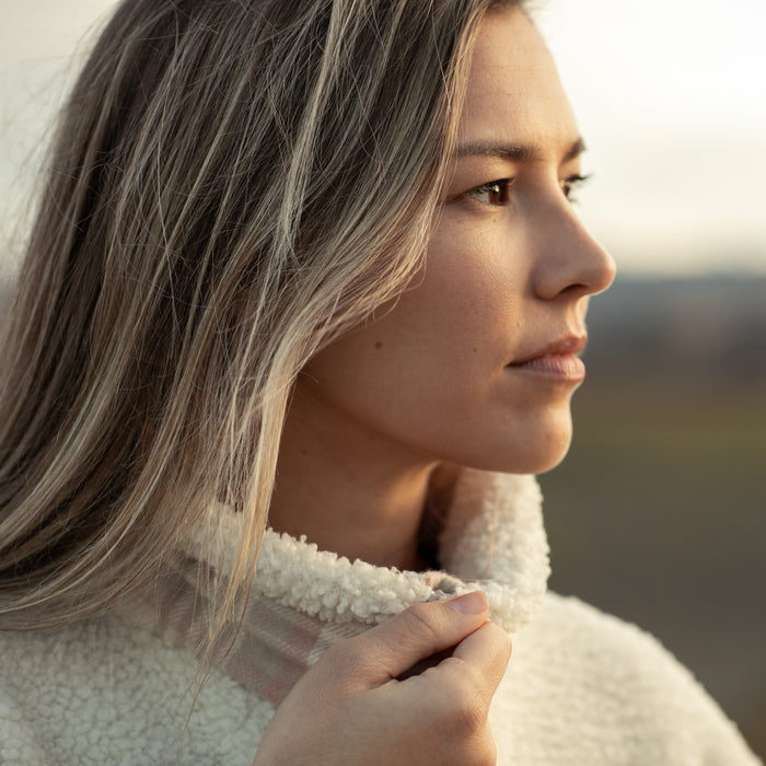 Woman with long hair in a Pladra Women's Jenner Sherpa Fleece - Oatmeal White gazes thoughtfully outdoors.