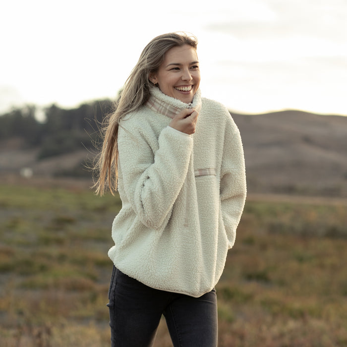 Smiling woman wears the Pladra Women's Jenner Sherpa Fleece in Oatmeal White, standing outdoors by grassy hills.