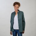 Woman in Pladra Women's Leon Workhorse Shirt–Fir Green Pincord over a white tee and jeans, smiling against a plain background.