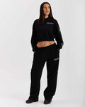 Person wearing a black tracksuit with brand logos on a white background
