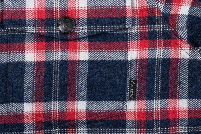 Close-up of a Women's Northwood Sherpa Insulated Flannel Jacket in Eagle Blue, featuring a button and a small black fabric tag labeled PALDRA sewn on the pocket.