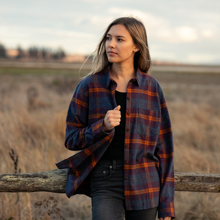 Woman wears Pladra Women's Relaxed Every Day Flannel Shirt in Portsmouth Blue Heather, leaning on a fence in a field.