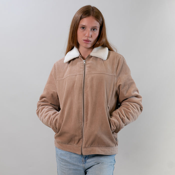 Woman with long hair wears a Pladra Women's Stinson Jacket–Oak Tan and blue jeans, standing against a plain background.