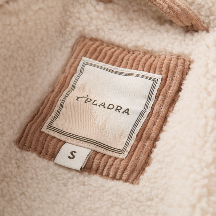 A close-up of a Pladra S tag on the Women’s Stinson Jacket in Oak Tan, featuring cream fleece and corduroy patch.