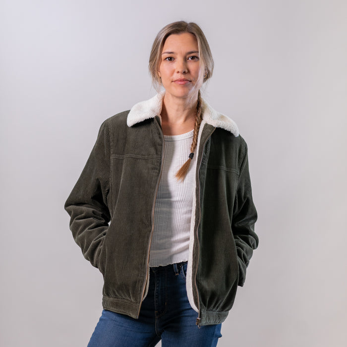 Women's Stinson Jacket in Pine Green, a sherpa-lined cotton corduroy jacket with a white fleece collar, worn with blue jeans.