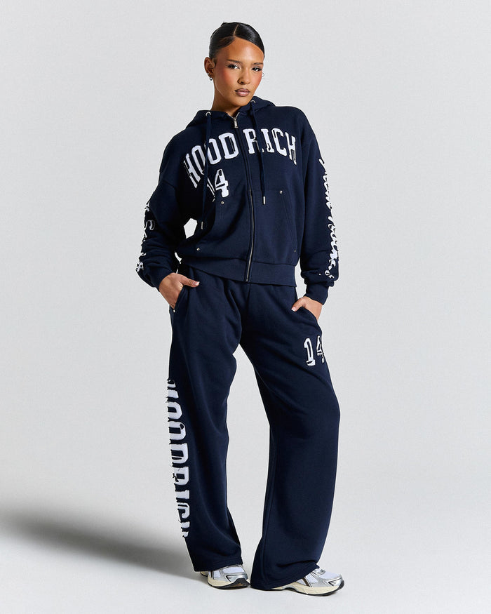 Person wearing a navy tracksuit with 'Hood Rich' branding on a light gray background
