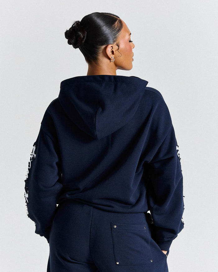 Person wearing a navy blue hoodie with white text on sleeves against a light gray background