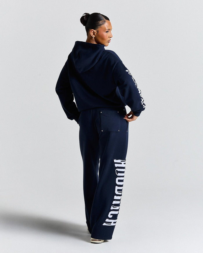 Person wearing a navy tracksuit with branding on a light gray background