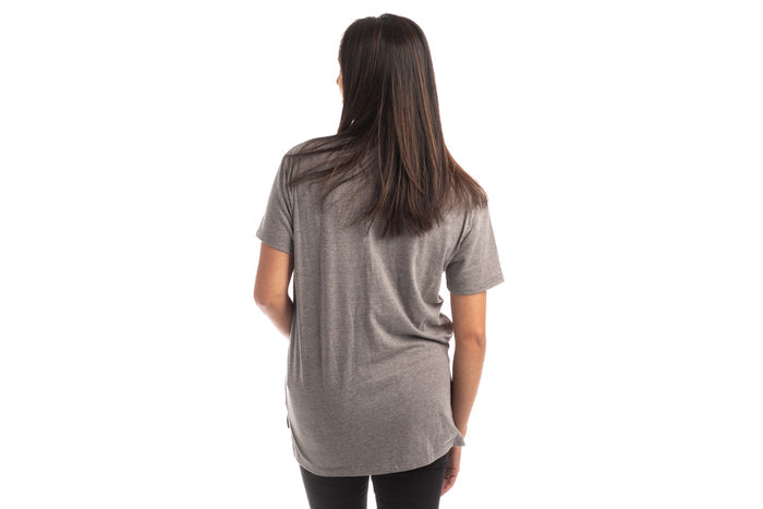 A woman with straight dark hair faces away from the camera, wearing a Women's V-Neck Tri-Blend Tee in Charcoal Grey Heather and black pants, set against a white background.