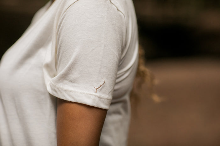 Outdoors in a Pladra Women's V-Neck Tri-Blend Tee—Marshmallow White Heather, logo on the sleeve.