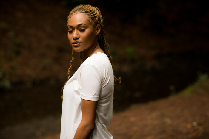 Woman with braided hair wears a Pladra Women's V-Neck Tri-Blend Tee in Marshmallow White Heather, gazing serenely outdoors.
