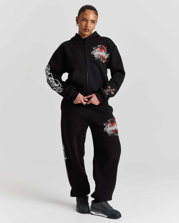Person wearing a black hoodie and pants with floral designs on a white background