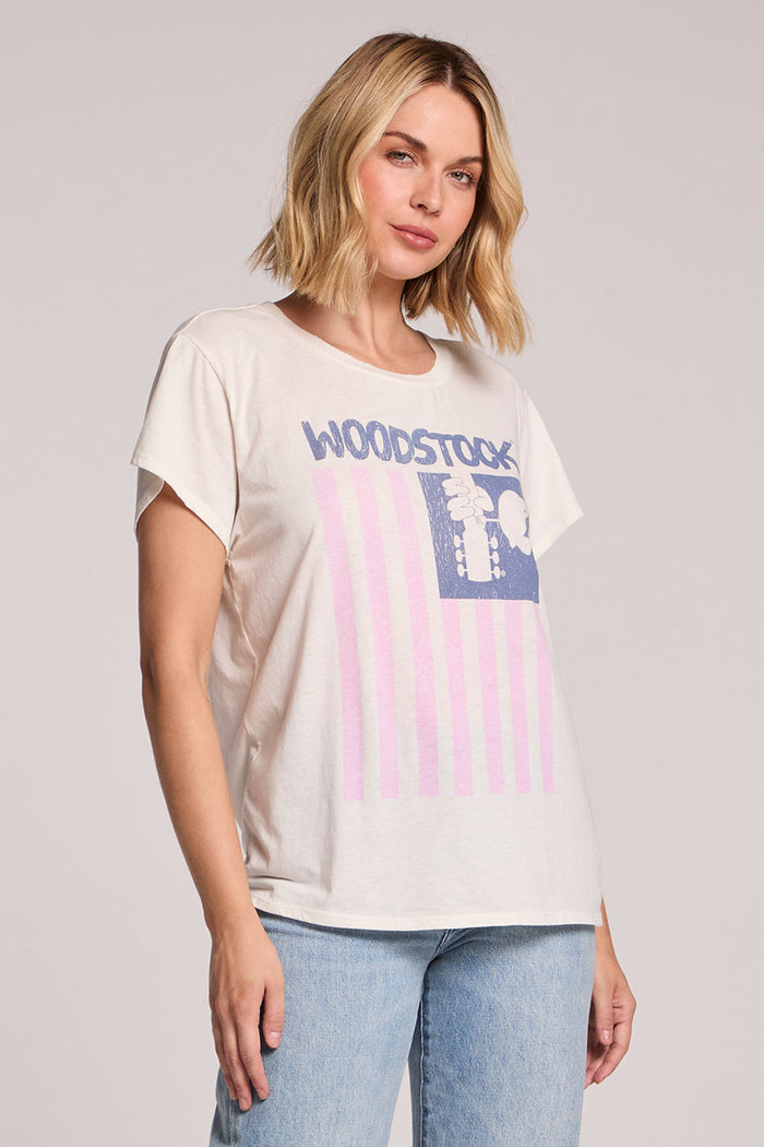 Side angle view of a woman wearing the Chaser Woodstock American Flag Tee on a neutral background with hands at her sides