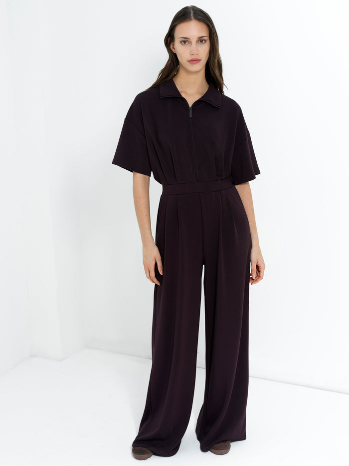 Woman wearing a brown half zip jumpsuit with short sleeves wide leg trousers an elasticated waist two side pockets and a relaxed fit.