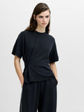 A woman wearing a dark grey relaxed fit T-shirt with a cinched waist, dropped shoulders, a crew neck and short sleeves.