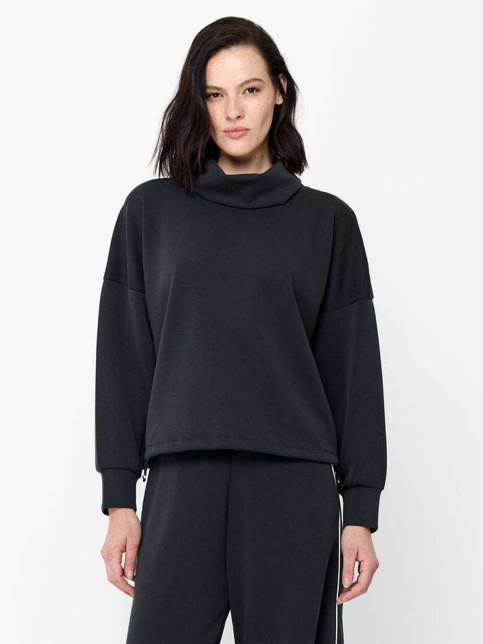 A woman wearing a dark grey sweatshirt with a dropped funnel neckline, adjustable toggles and long cuffed sleeves.
